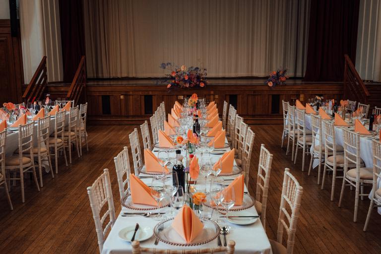 long tables dressed for wedding breakfast with cream chairs and orange napkins