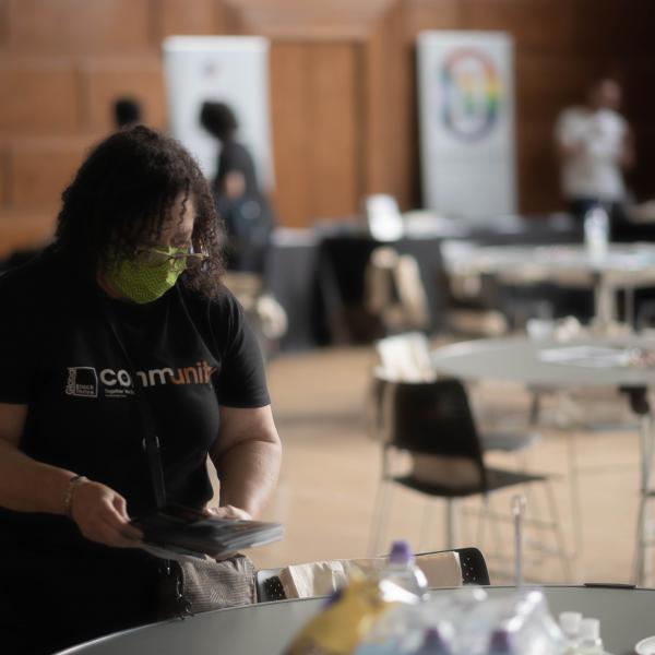 Black Thrive staff member in branded t-shirt placing information leaflets onto grey tables at community event 