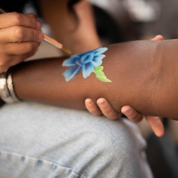 Professional face-painter paints a blue flower onto the forearm of another person