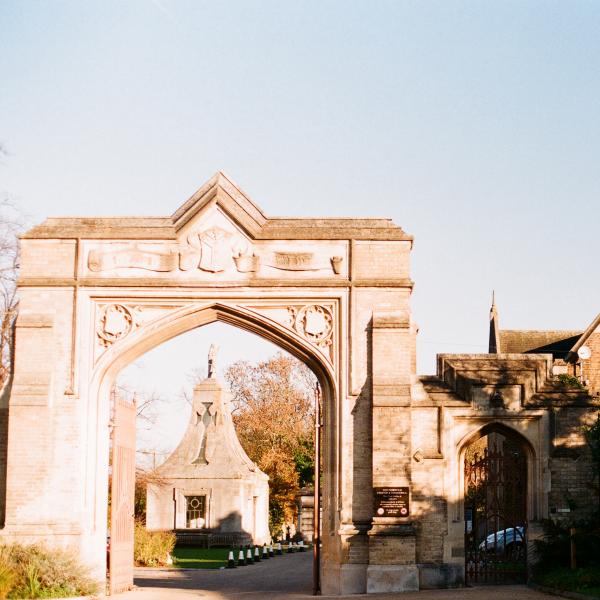 Gated archway of West Norwood Cemetery with sun shining to the left and the right of the image in shadow. Blue skies in background