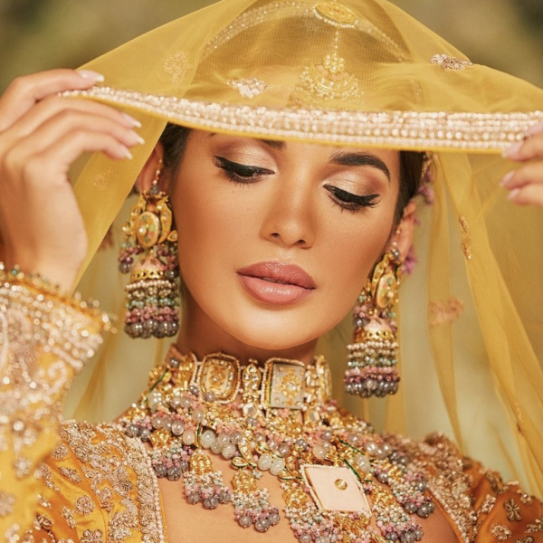 Woman holding yellow and gold veil wearing intricate purple and gold jewellery  