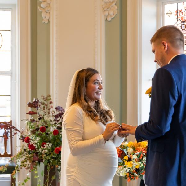Couple exchanging rings in the Circular Hall, with flowers and stained glass windows in the background
