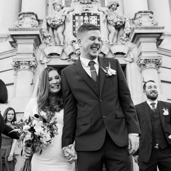 Black & White image of newlyweds leaving Lambeth Town Hall with friends and family behind 