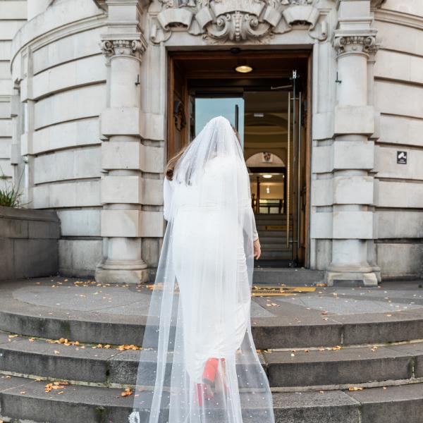 Bride in white dress walking up stairs into Lambeth Town Hall with lace veil flowing behind her