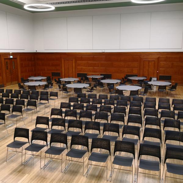 rows of black chairs and round tables with chairs in Assembly Hall with wooden floors 